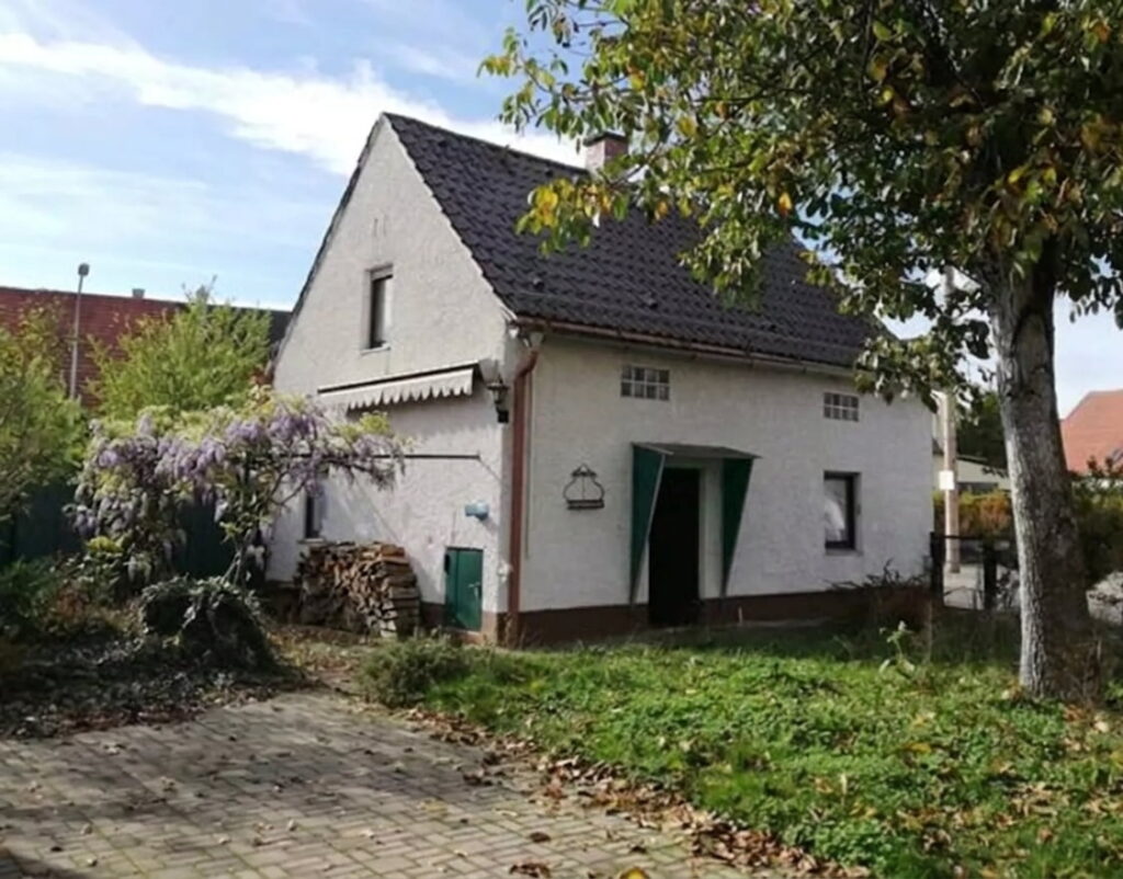 Einfamilienhaus mit Satteldach, weißer Fassade und grünem Eingang in einem Garten mit Baum und gepflastertem Weg