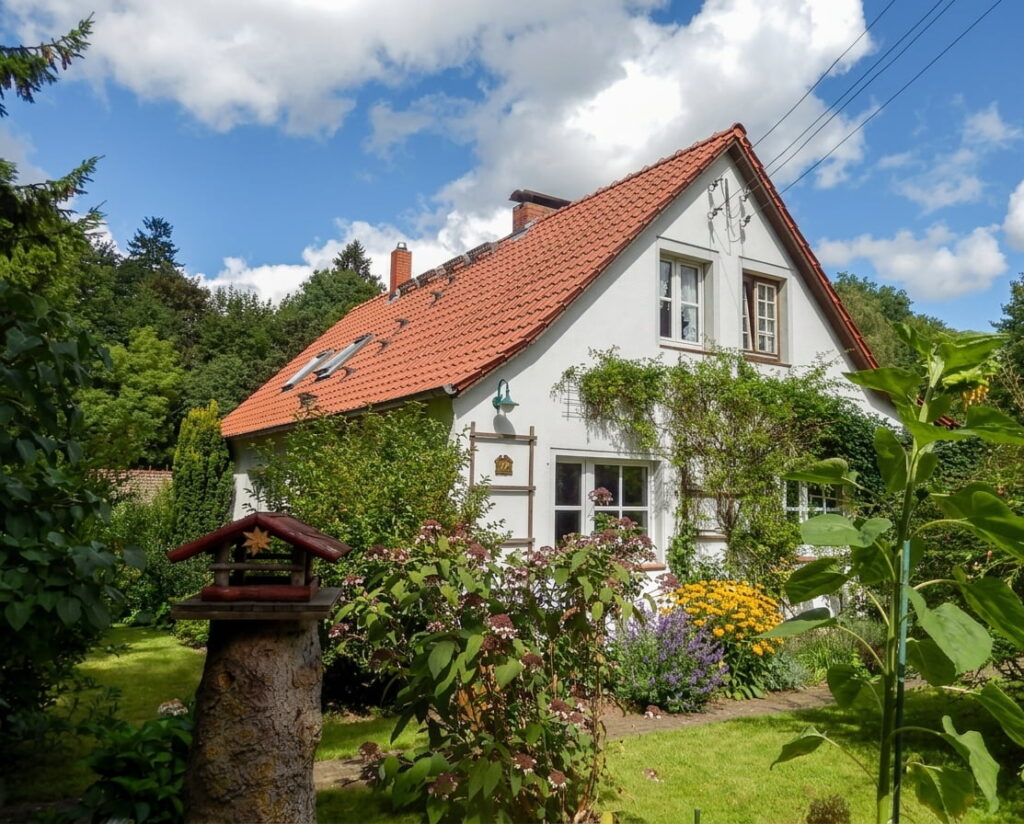 Einfamilienhaus mit rotem Satteldach und weißer Fassade umgeben von üppigem Garten mit Blumen und Büschen im Lehel