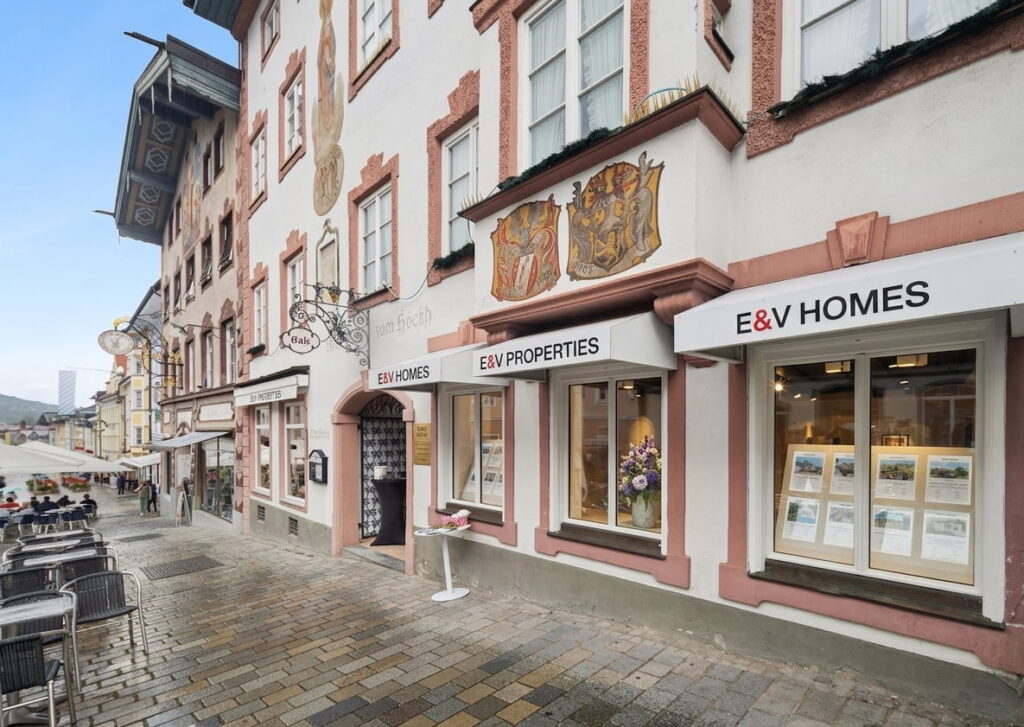Straßenszene mit historischen Gebäuden und Schildern von E&V HOMES und E&V PROPERTIES an einem Haus in der Ludwigsvorstadt