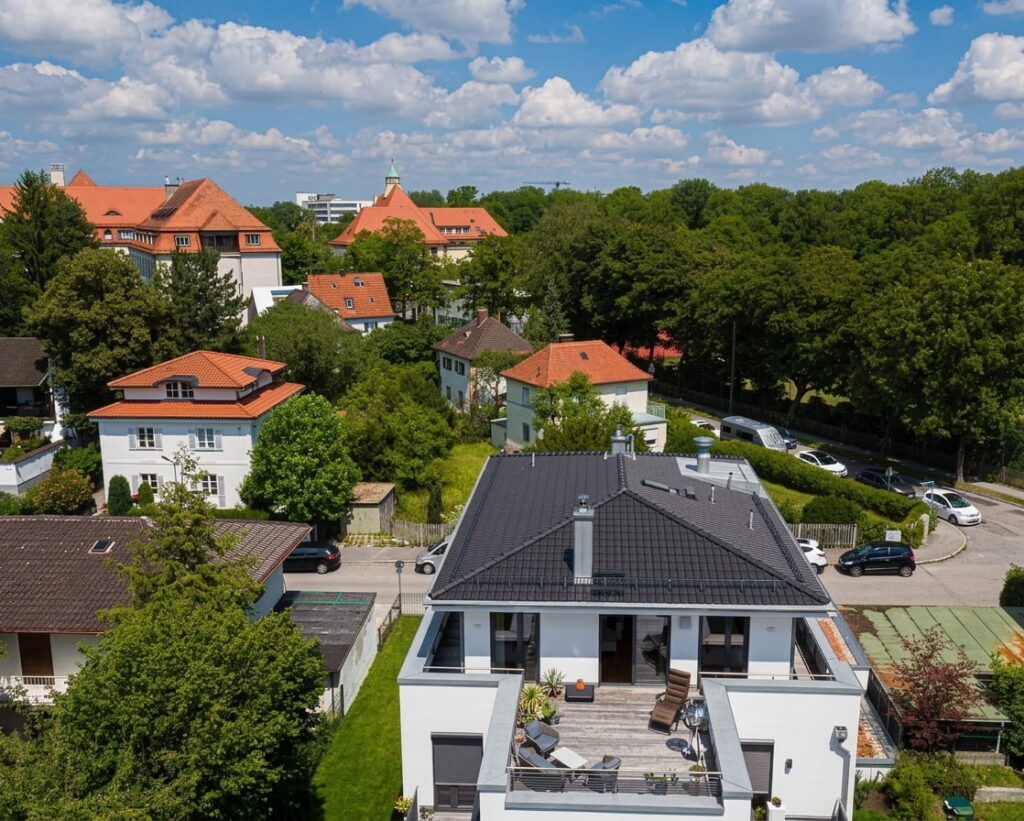 Luftaufnahme eines modernen weißen Hauses mit großer Dachterrasse in einem grünen Wohnviertel mit weiteren Häusern und Bäumen in Ludwigsvorstadt