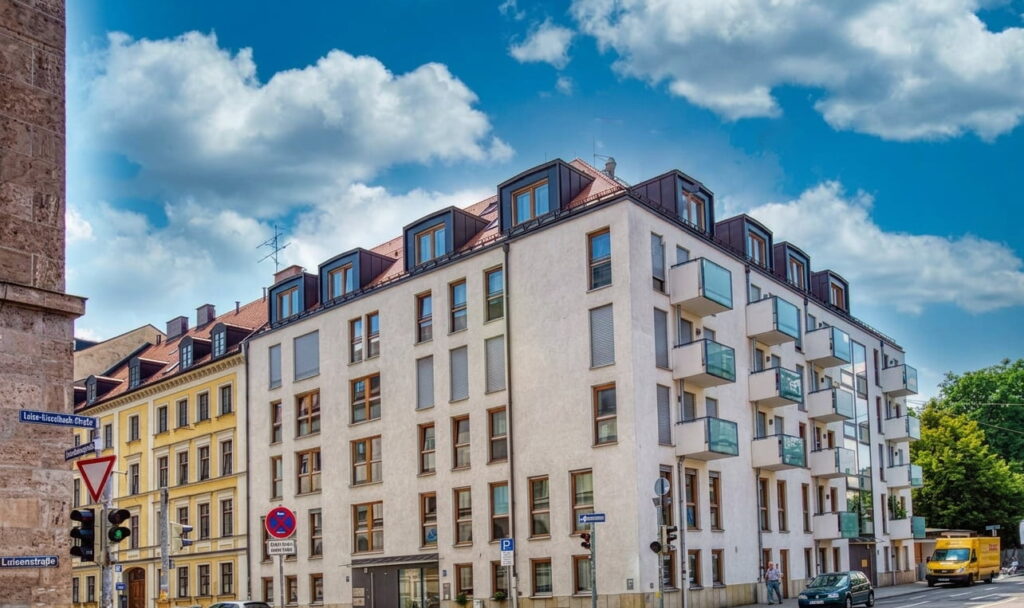 Mehrstöckiges Wohnhaus an einer Straßenecke in einem städtischen Viertel mit blauem Himmel und Wolken