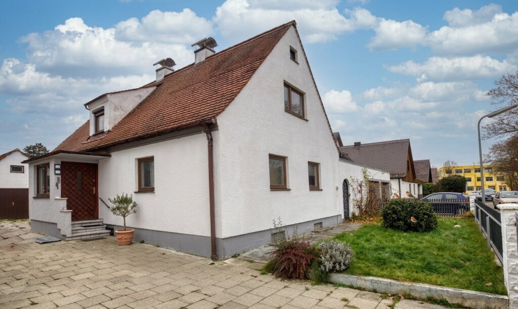 Einfamilienhaus mit weißer Putzfassade und rotem Satteldach in einer Wohnsiedlung mit Vorgarten und gepflastertem Eingangsbereich