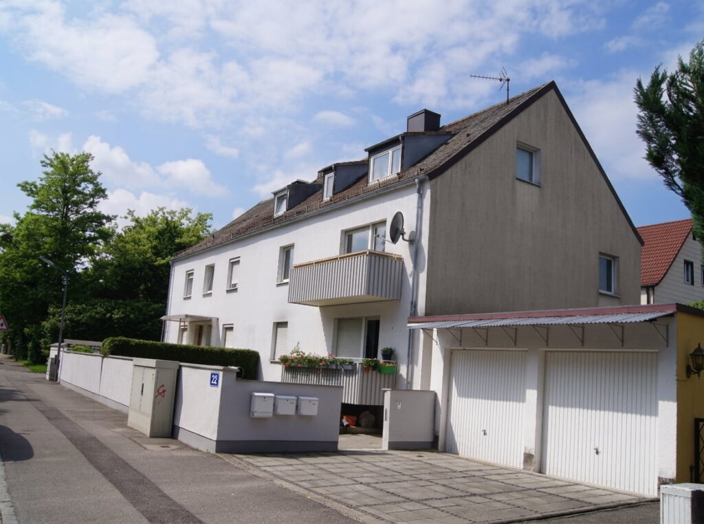 Zweistöckiges Wohnhaus mit Satteldach, Balkon und angrenzender Garage an einer ruhigen Straße in Moosach