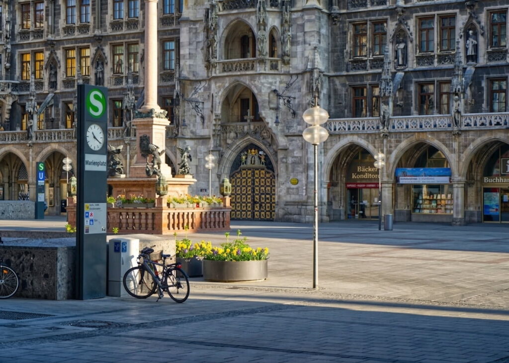 Blick auf den Marienplatz in München mit dem historischen Rathaus, einer S-Bahn-Station und einem Fahrrad an einem Poller