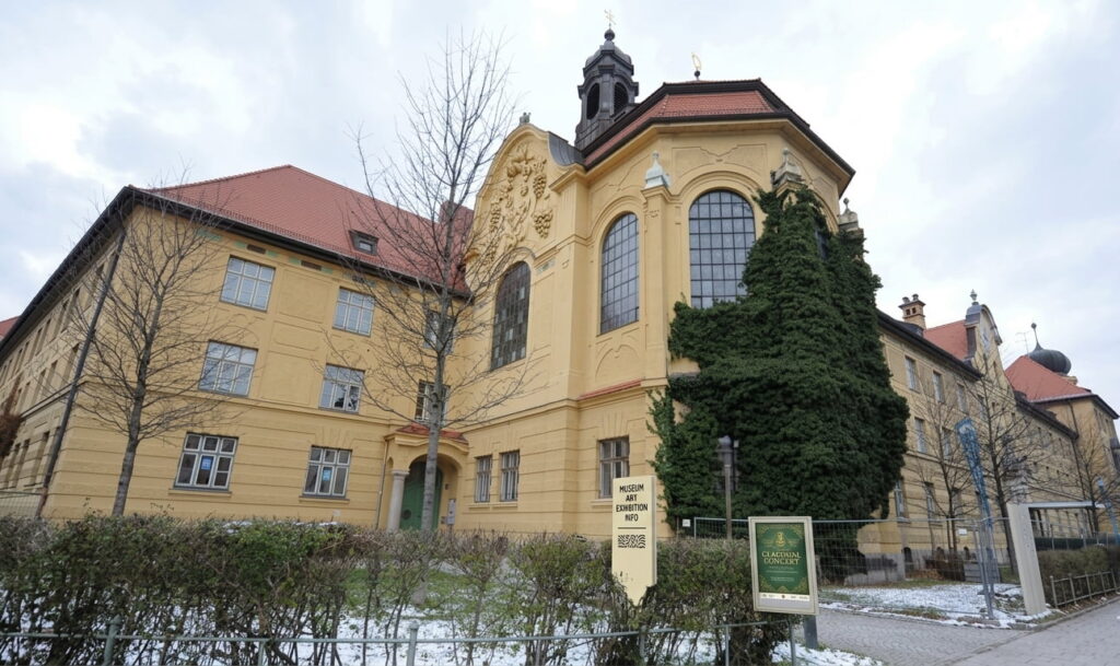 Großes historisches Gebäude mit gelber Fassade, roten Dächern und einer mit Efeu bewachsenen Ecke in Obergiesing