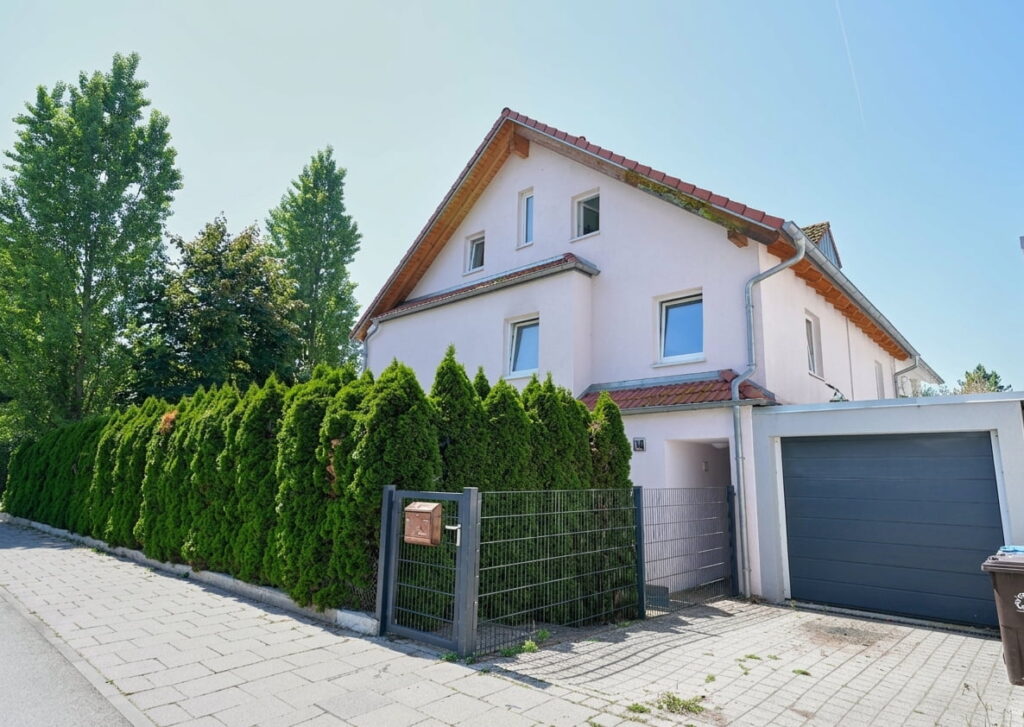 Zweistöckiges Einfamilienhaus mit Satteldach, Garage und Hecke an einem Gehweg in Obergiesing
