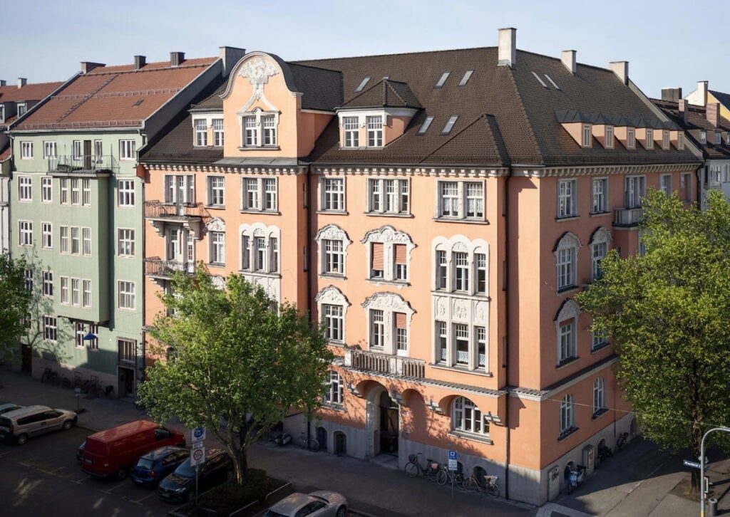 Mehrstöckiges Wohnhaus mit historischer Fassade und Erkern in einem Stadtviertel mit weiteren Altbauten und parkenden Autos in Schwabing