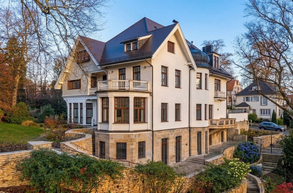 Großes, mehrstöckiges Wohnhaus mit Satteldach und mehreren Fenstern, umgeben von Garten und Bäumen in einem Wohngebiet