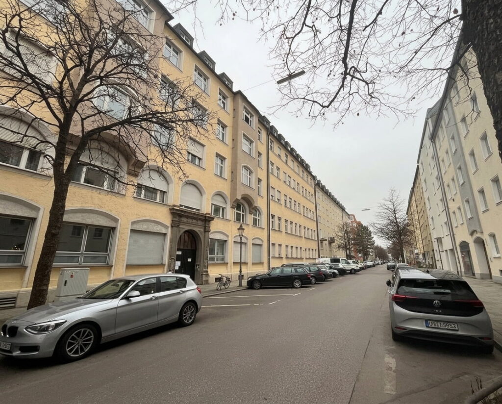 Straße in Haidhausen mit geparkten Autos und mehrstöckigen Wohngebäuden bei bewölktem Himmel