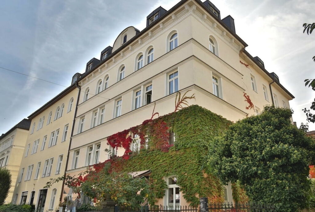 Mehrstöckiges Eckgebäude mit weißer Fassade und teilweise mit Efeu bewachsen in der Isarvorstadt