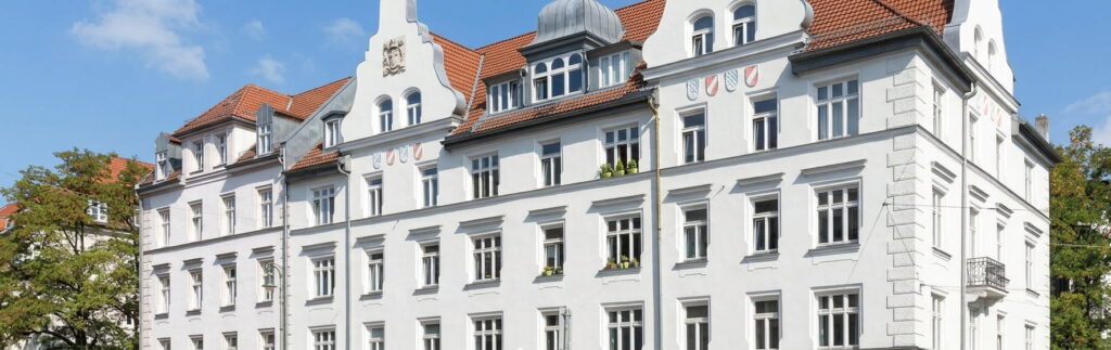 Mehrstöckiges historisches Wohngebäude mit weißer Fassade, roten Ziegeldächern und mehreren Gauben unter blauem Himmel in Schwabing-West