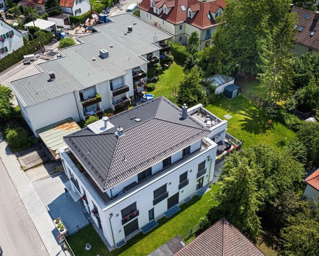 Luftaufnahme eines Wohngebäudes mit Flachdach und angrenzendem Garten in einem Wohnviertel mit weiteren Häusern und Bäumen