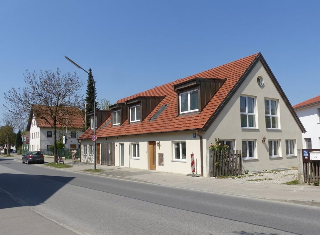 Einfamilienhaus mit rotem Satteldach und mehreren Dachgauben an einer ruhigen Straße in Trudering