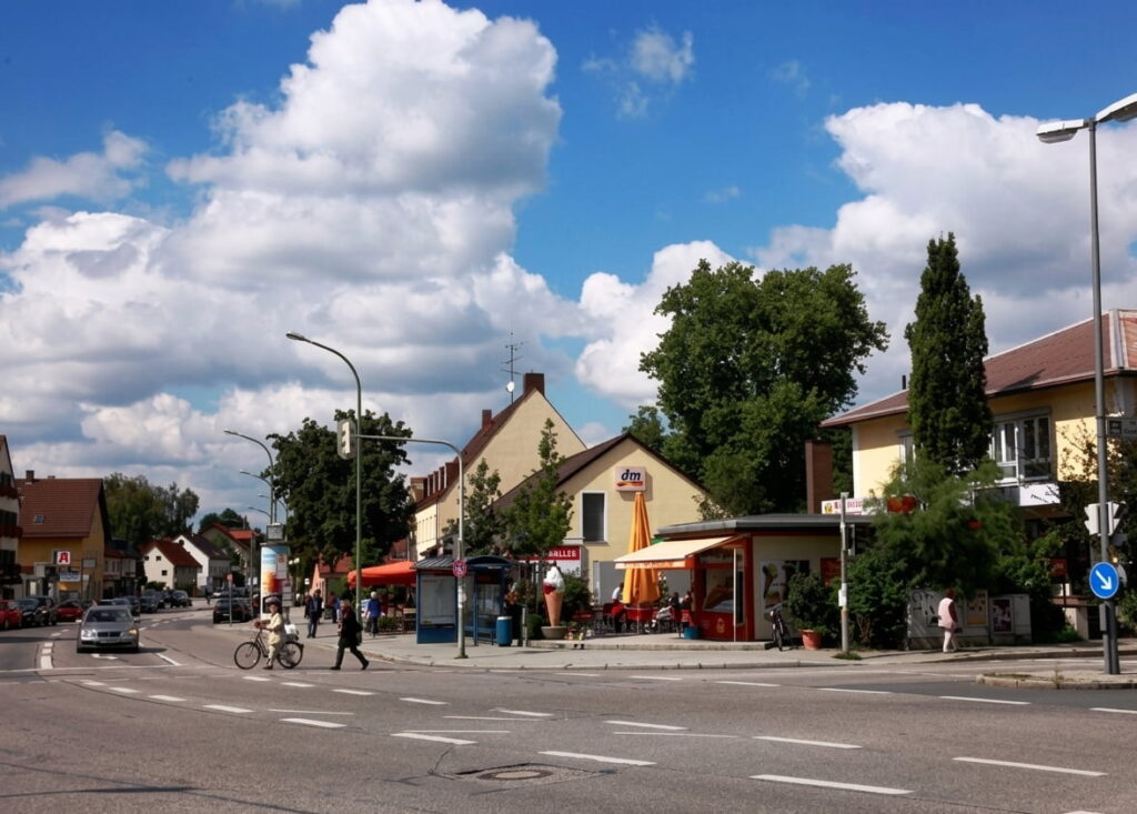 Straßenszene in Trudering mit Wohnhäusern, einem dm-Markt, Fahrradfahrern und Fußgängern bei blauem Himmel mit Wolken