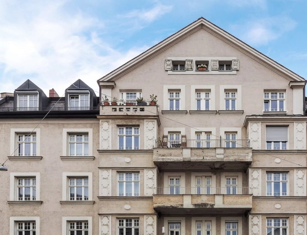 Fassade eines mehrstöckigen Wohngebäudes mit mehreren Fenstern, Balkonen und einem Giebeldach in Bogenhausen