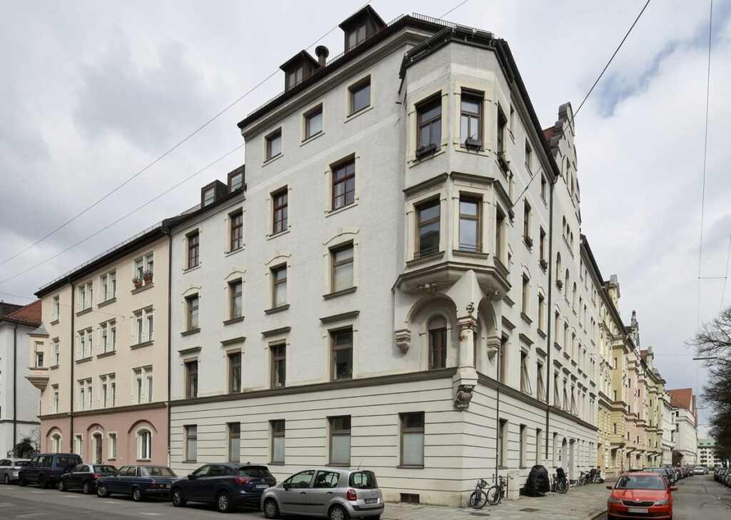 Mehrstöckiges Eckgebäude im klassischen Stil mit mehreren geparkten Autos und Fahrrädern in einer ruhigen Wohnstraße