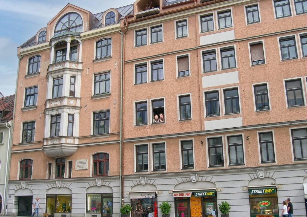 Luftaufnahme eines historischen Gebäudekomplexes mit roten Ziegeldächern und Innenhof im Stadtteil Maxvorstadt mit Blick auf die Türme der Theatinerkirche im Hintergrund