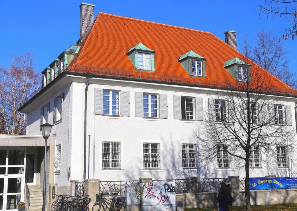 Zweigeschossiges Wohngebäude mit rotem Satteldach, weißen Fensterläden und mehreren Dachgauben in Milbertshofen