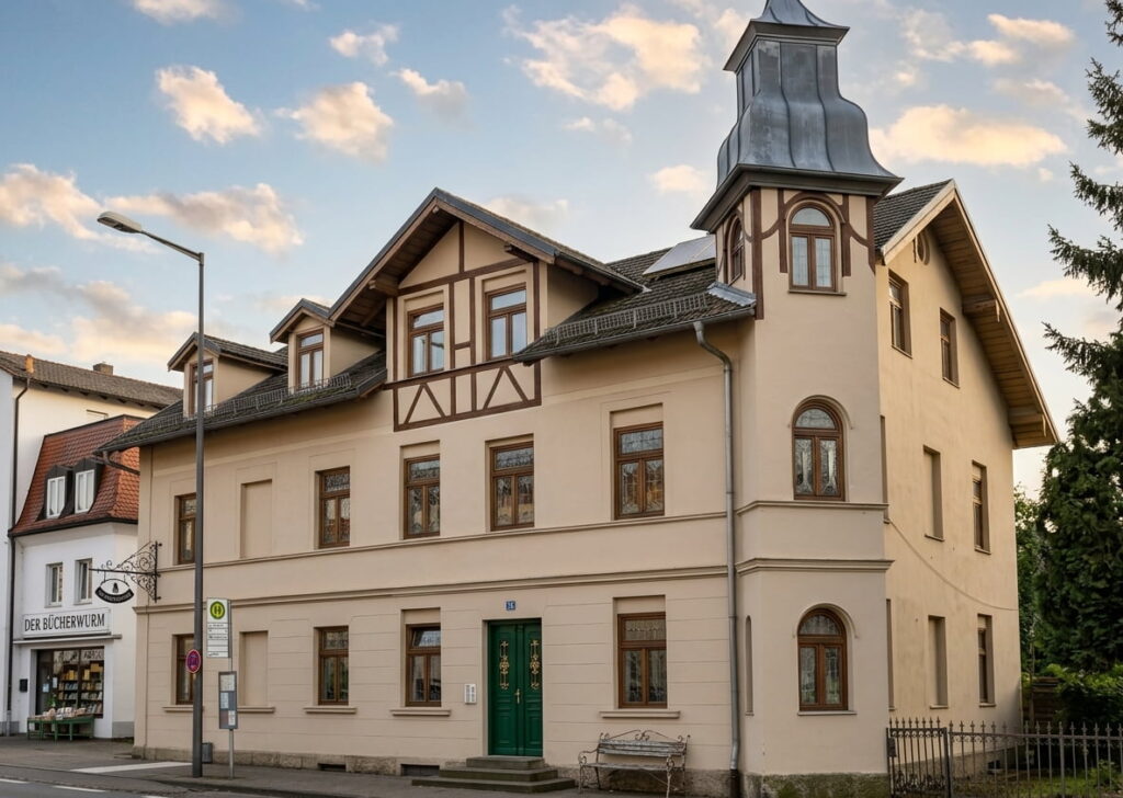 Zweistöckiges historisches Gebäude mit grünem Eingang, Erker mit Turm und Laden mit Schriftzug 'DER BÜCHERWELT' an der Straßenecke in Moosach