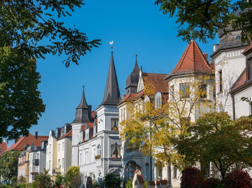 Reihe historischer Wohnhäuser mit spitzen Türmen und roten Dächern vor blauem Himmel in Neuhausen