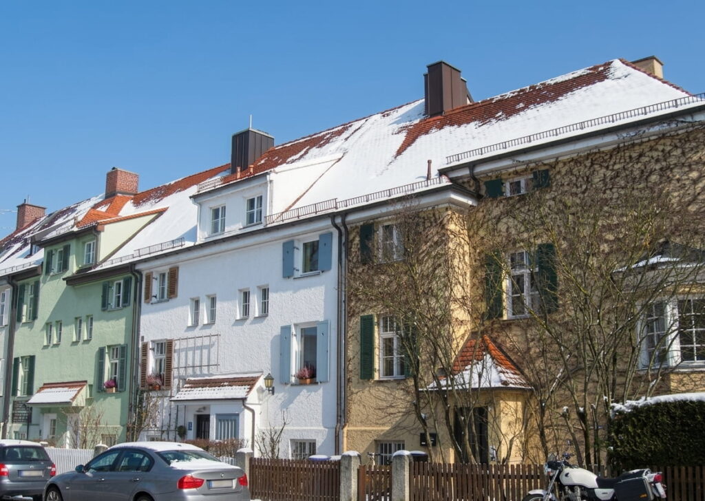 Reihe von mehrstöckigen Wohnhäusern mit verschneiten Dächern und parkenden Autos in einer ruhigen Straße in Nymphenburg