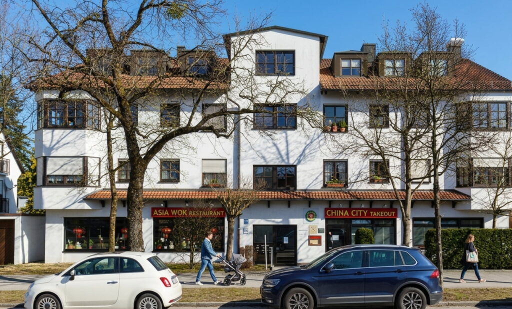 Mehrstöckiges Wohn- und Geschäftshaus mit zwei Restaurants im Erdgeschoss, davor zwei parkende Autos und drei Fußgänger auf dem Gehweg