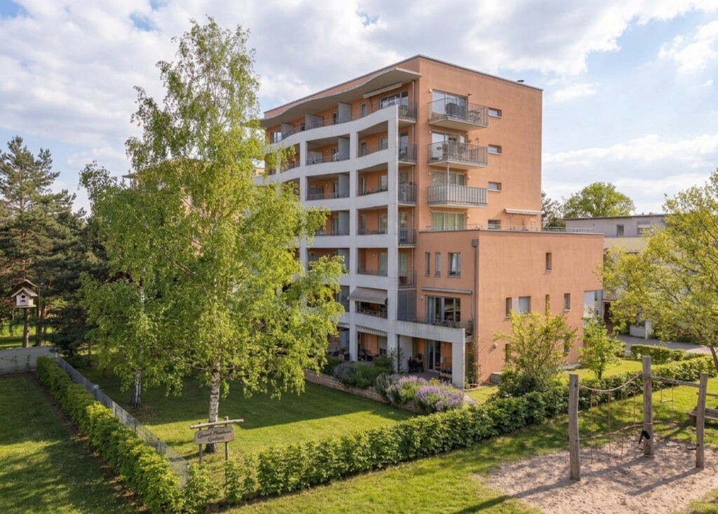 Mehrstöckiges Wohngebäude mit Balkonen, umgeben von Bäumen und einem kleinen Spielplatz im Vordergrund