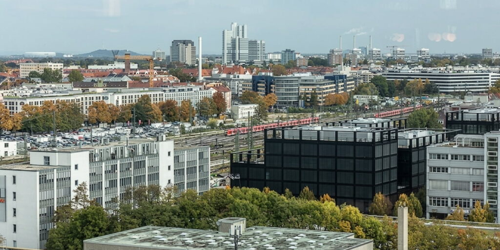 Städtische Ansicht mit Wohn- und Bürogebäuden, Bäumen und einem Zug in Berg am Laim