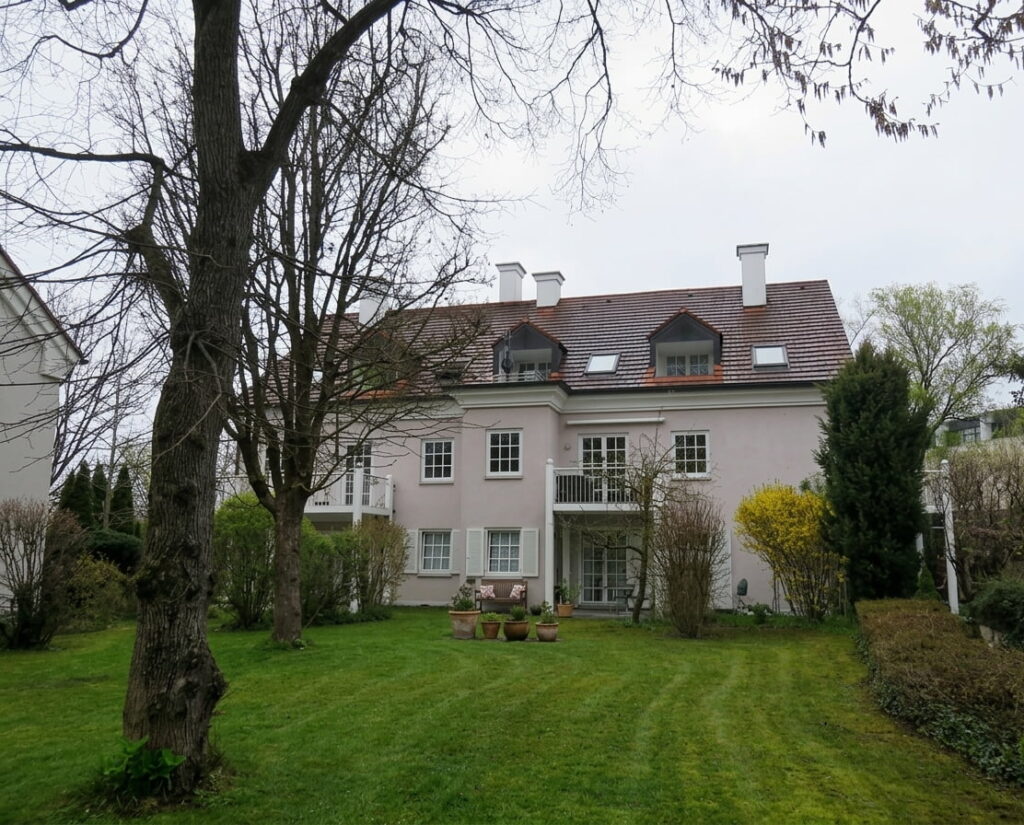 Mehrstöckiges Wohnhaus mit Satteldach und Balkonen, umgeben von gepflegtem Garten mit Rasen und Bäumen im Fasangarten