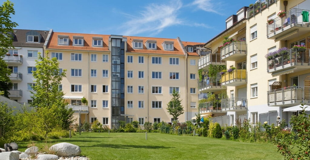 Mehrstöckige Wohngebäude mit Balkonen und gepflegter Grünfläche im Innenhof bei sonnigem Wetter