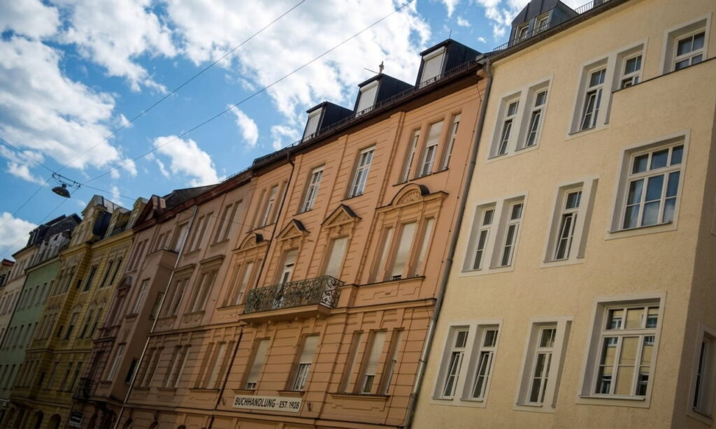 Mehrere mehrstöckige Altbauten mit klassischer Fassadengestaltung und Dachgauben unter blauem Himmel mit Wolken
