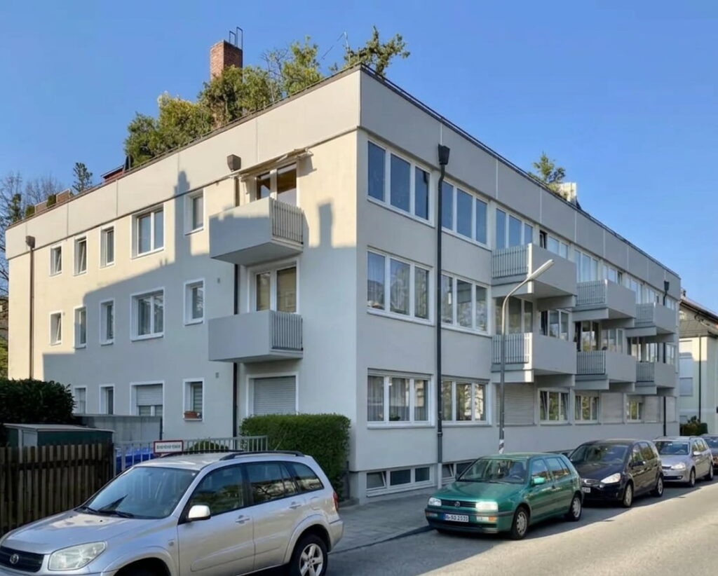 Mehrstöckiges Wohnhaus mit Balkonen an der Straßenseite und mehreren parkenden Autos davor