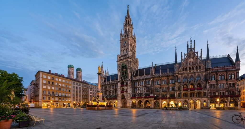 Blick auf den beleuchteten Marienplatz mit dem Neuen Rathaus und den Türmen der Frauenkirche im Abendlicht in München