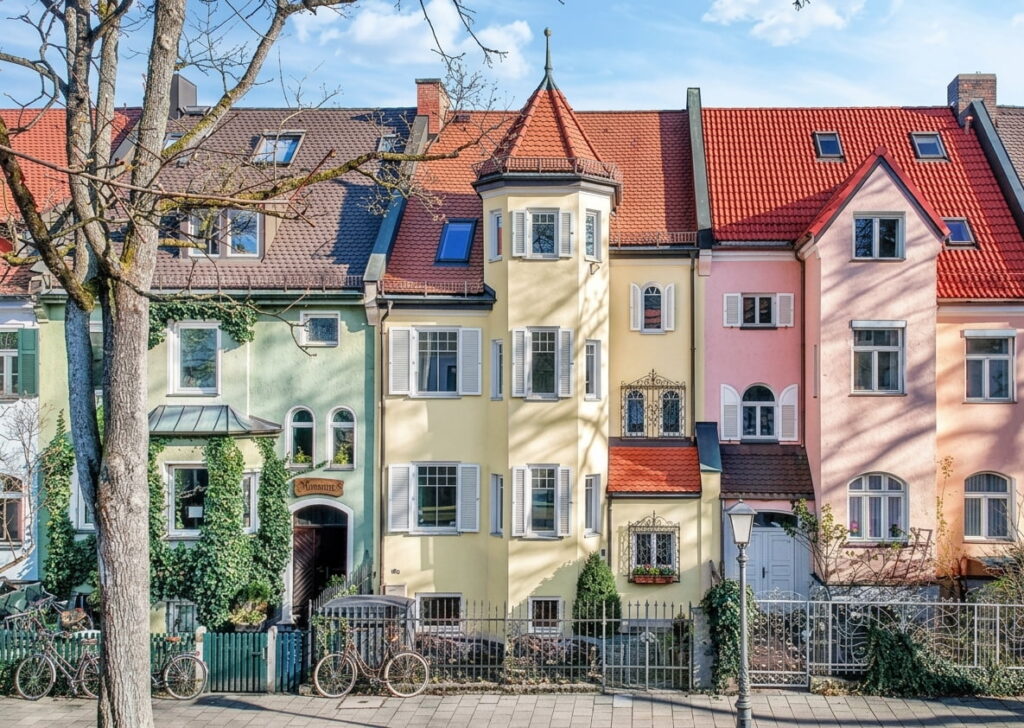 Reihe von mehrstöckigen Altbauten mit Giebeldächern und Erkern in einem Wohnviertel mit Bäumen und Fahrrädern davor