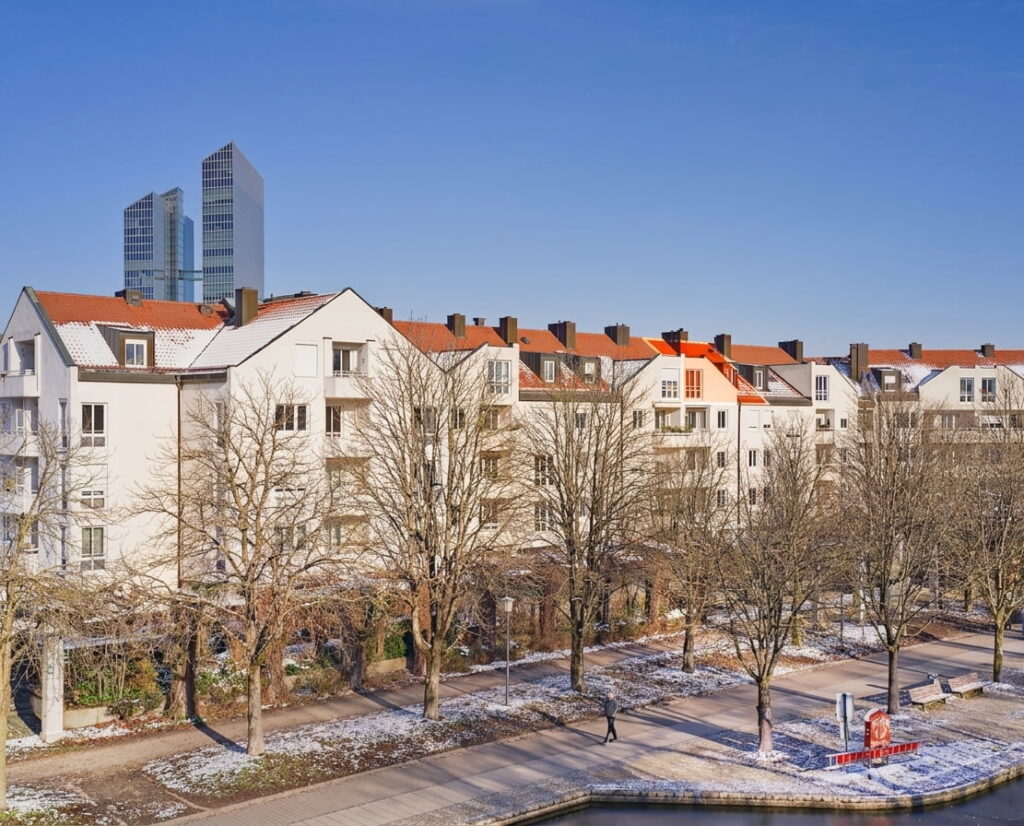 Mehrere mehrstöckige Wohngebäude mit roten Dächern an einem Wasserkanal im Stadtteil Schwabing bei klarem Himmel und leichtem Schneefall