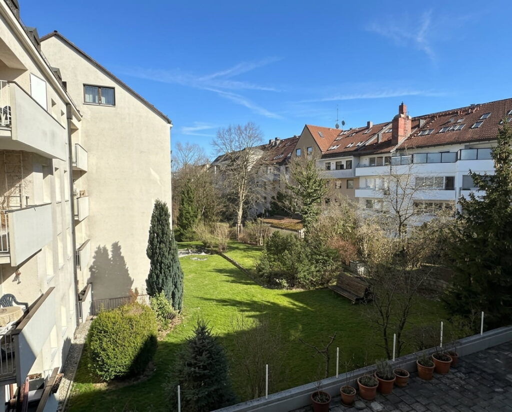 Blick auf einen begrünten Innenhof mit Bäumen, Sträuchern und einer Bank zwischen Wohngebäuden in Sendling