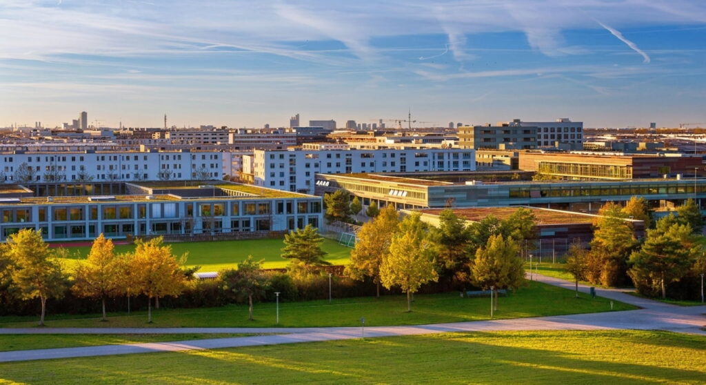 Weitwinkelaufnahme eines modernen Wohngebiets mit mehrstöckigen Gebäuden, umgeben von grünen Wiesen und Bäumen unter blauem Himmel