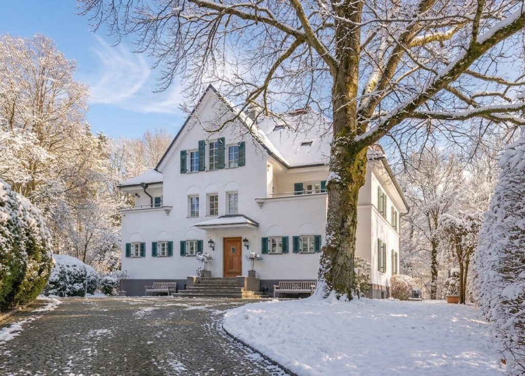Großes weißes Landhaus mit grünen Fensterläden und verschneitem Garten im Winter